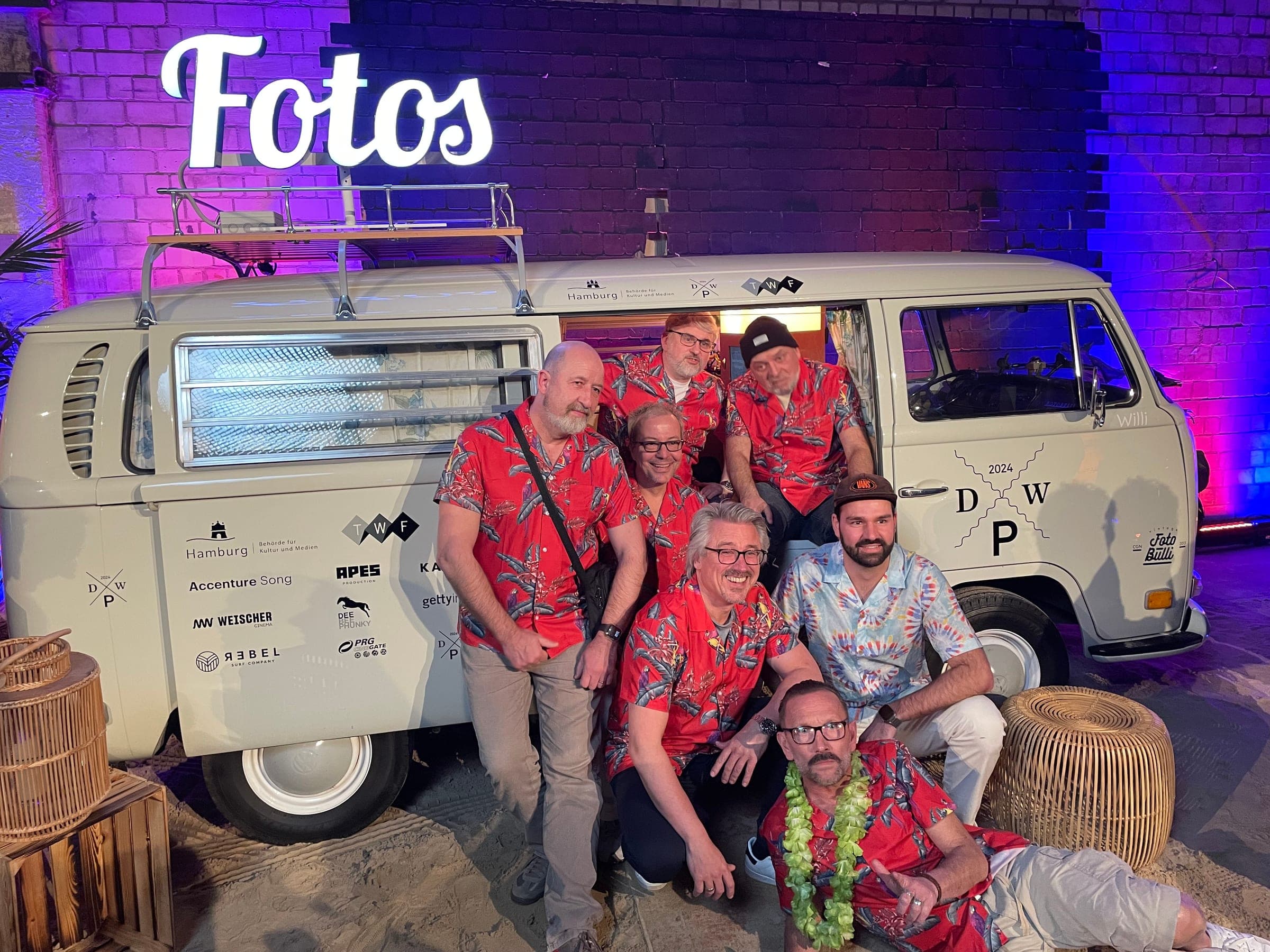 Der Fotobulli Willi mit leuchtendem Fotos-Schriftzug bei einer abendlichen Preisverleihung in Hamburg, davor eine Gruppe in Hawaiihemden
