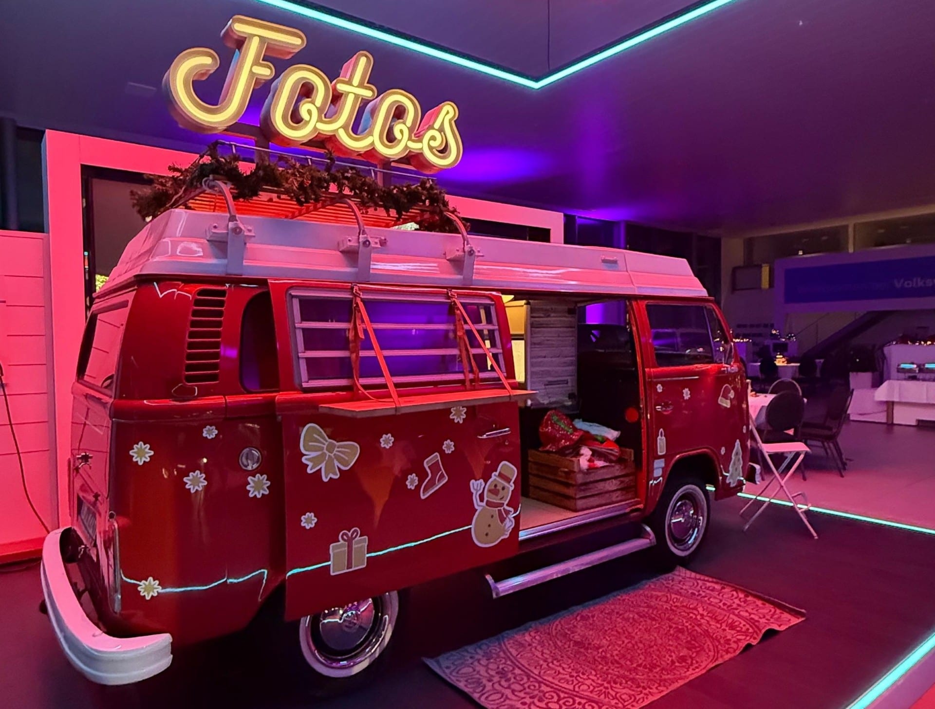 Der rote XMAS-Fotobulli mit Tannengrün auf dem Dachträger, Schneemann- und Geschenk-Aufklebern und offener Seitentür mit Requisitenkiste in einer Eventhalle