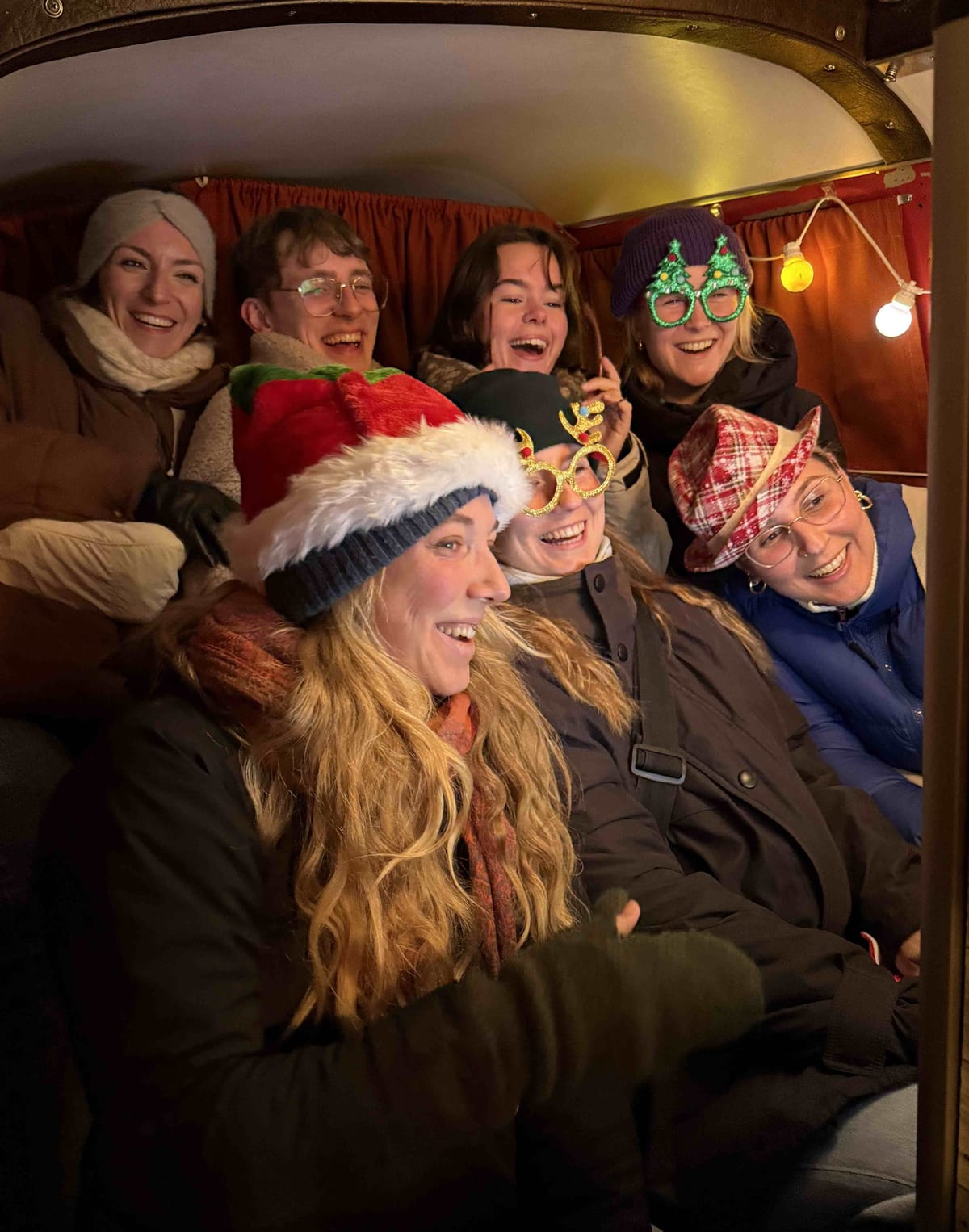 Gäste mit Weihnachtsmützen und Rentier-Brillen lachen auf der Rückbank des XMAS-Fotobullis